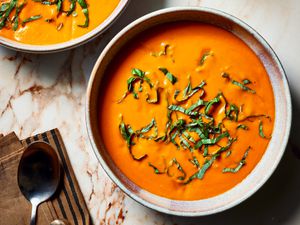 Overhead view of two bowls of tomato soup with shredded greens on top