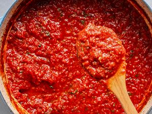 A pot of tomato sauce with a wooden spoon lifting some sauce