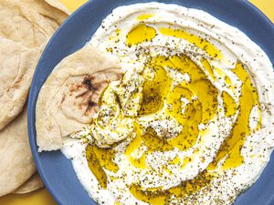 Overhead view of labaneh on a plate drizzled with olive oil, sprinkled with salt and pepper, and served with pita bread.