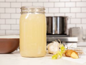 Side view of pork stock in a jar next to ginger and garlic
