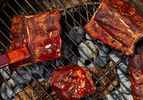 Barbecue ribs and meat on a grill with sauce being applied