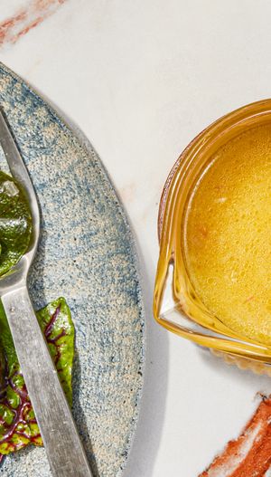 Lemon vinaigrette in a small bowl next to a plate of greens.