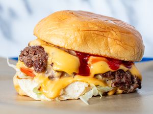A cheeseburger with melted cheese lettuce tomato ketchup and a soft toasted bun