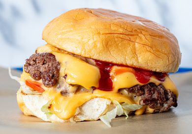A cheeseburger with melted cheese lettuce tomato ketchup and a soft toasted bun