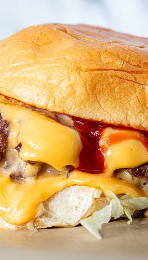A cheeseburger with melted cheese lettuce tomato ketchup and a soft toasted bun