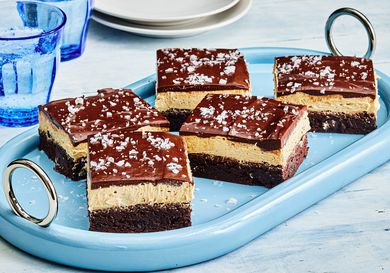 Buckeye Brownies with sea salt garnish, cut into pieces on a blue dish, with blue cups and small white plates
