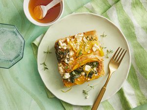 slice of savory crinkle pie on a plate with green textiles, a sparkling water, and a small bowl of honey on the side