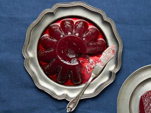 Silver platter of jellied cranberry sauce with a small plate of cranberry sauce in the bottom corner