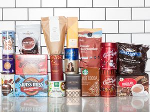 group of different hot chocolate packages stacked together on white surface with white tile background