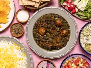 Overhead of Khoresh E Ghormeh Sabzi surrounded with rice, dips, and vegetables