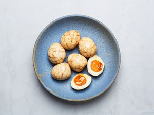 blue bowl of marbled tea eggs, with one sliced open, yolks showing