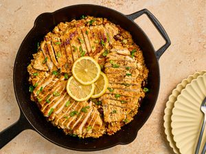 Chicken with bulgar in a skillet, garnished with lemon and chives, with pale yellow plates on the side