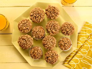 banana nut muffins on a yellow platter, with yellow napkins, a yellow tabletop and orange juice