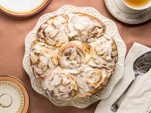 overhead of frangipane rolls on white platter, with 2 cups of tea on a pink tablecloth