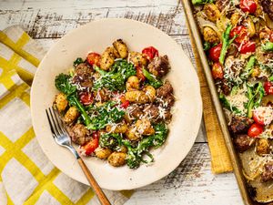 A plate of gnocchi with roasted vegetables and cheese, next to a sheet pan with more of the dish