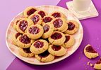 A plate of thumbprint cookies with jam filling next to a glass of milk and one partially eaten cookie