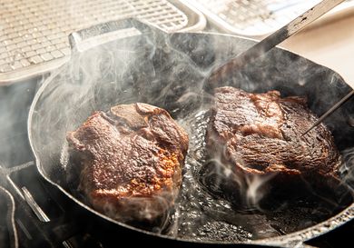 Two steaks cooking in a cast iron skillet with steam rising up
