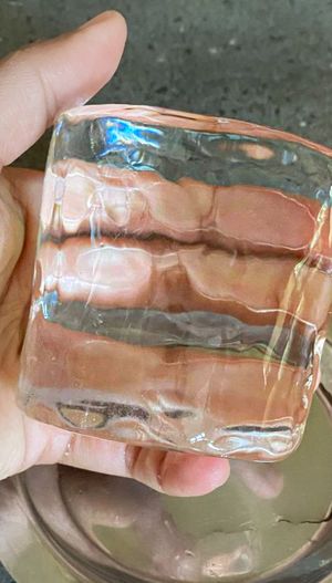 A hand holding a clear squareshaped ice cube over a reflective surface