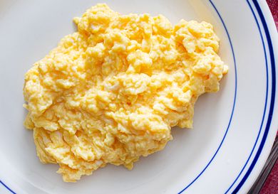 Scrambled eggs served on a white plate with a blue trim