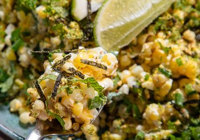 A dish of corn salad with herbs lime wedge garnish and nori strips visible