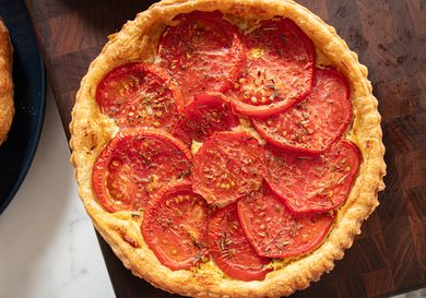 A tomato tart on a wooden surface consisting of a pastry crust layered with sliced tomatoes