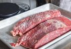 Salt being sprinkled on two raw beef cuts on a tray