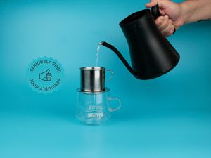 a hand pouring hot water from a kettle into a phin filter on a blue background