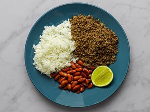 Salpicón, white rice, red kidney beans, and a slice of lime on a blue plate on a marble counter.