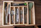 Kitchen utensils and flatware in a wooden drawer organizer.