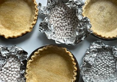A collection of baked pie crusts and pies filled with ceramic pie weights on a white surface.