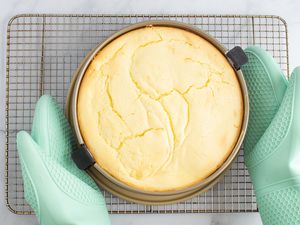 A person placing a springform pan onto a cooling rack