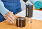 the comandante hand grinder with a cup of coffee next to it