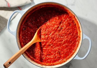 A pot of Italian-American tomato sauce in a dutch oven with a wooden spoon.