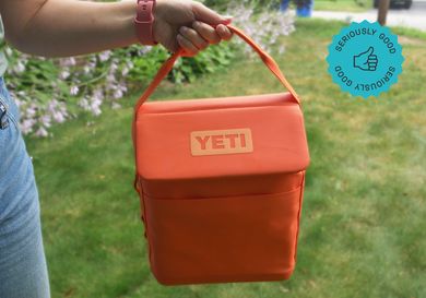 a person holding the handle on a bright orange yeti daytrip lunchbox