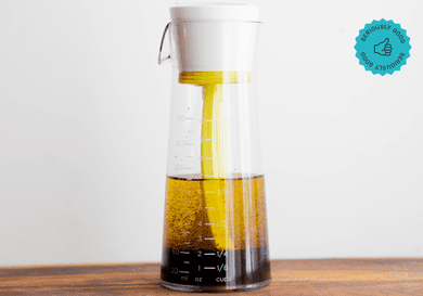 The Emulstir salad dressing mixer on a wooden table in front of a white wall.
